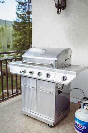 A stainless steel outdoor grill with four burners, a side cabinet, and a gas tank nearby.