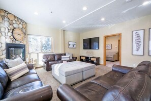A living room with a stone wall, leather sofas, a fireplace, and a TV.