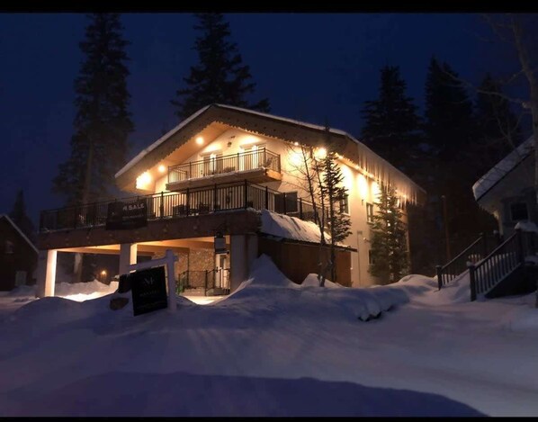 A two-story house with a balcony, surrounded by snow, at night.