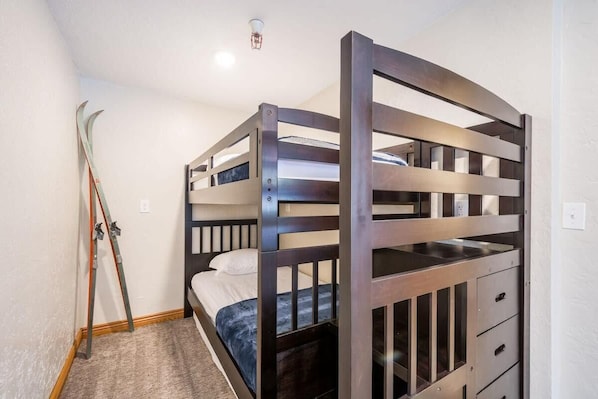 Habitación con literas, un cabecero de madera, un par de esquíes apoyados en la pared y suelo alfombrado.