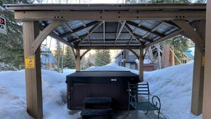 A covered outdoor area with a hot tub, a bench, and a caution sign warning of slippery conditions.