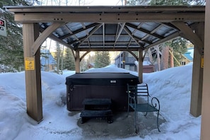 Un espace extérieur abrité comprenant un jacuzzi, un banc et un panneau d’avertissement indiquant que le sol est glissant.