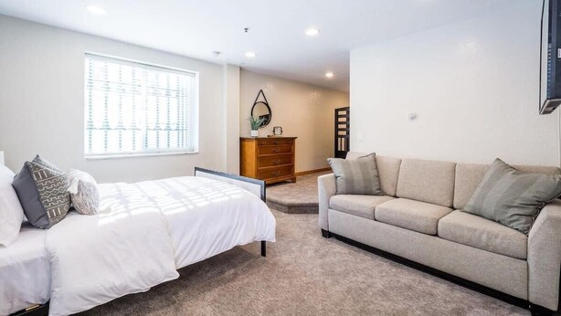 A bedroom with a bed, a sofa, a dresser, and a window.