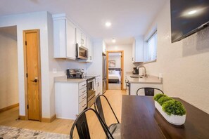 A compact kitchen with white cabinets, a microwave, and a dining area with a table and chairs.