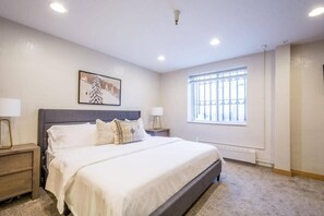 A bedroom with a large bed, two bedside tables, a window with bars, and a wall-mounted picture.