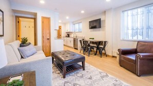A modern apartment with a living room, dining area, kitchenette, and a large window.