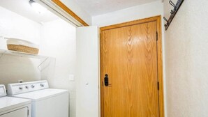 A laundry room with a wooden door, a washing machine, and a shelf with a basket.