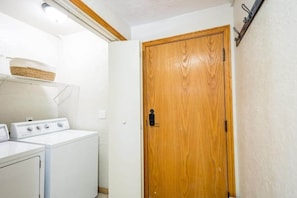 Une buanderie avec une porte en bois, un lave-linge et une étagère sur laquelle se trouve un panier.