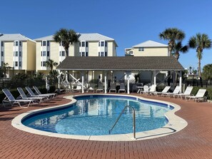 A swimming pool with lounge chairs and a covered seating area, surrounded by multi-story buildings.