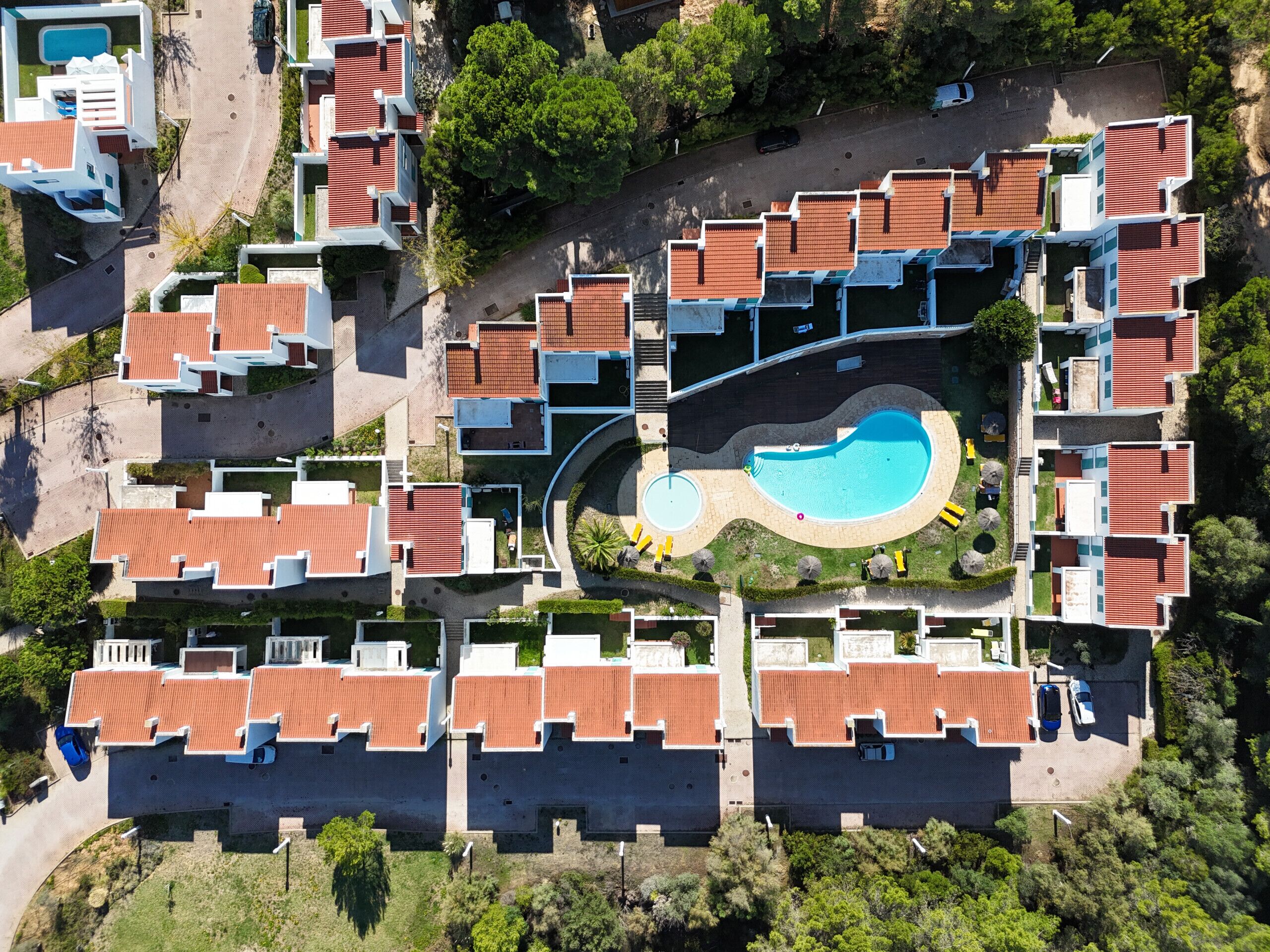 An aerial view of a residential complex with multiple buildings, a central swimming pool, and surrounding greenery.