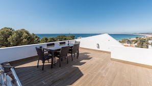 A rooftop terrace with a table and chairs, overlooking a coastal landscape. - Prainha Luxury Apartment (Alvor)