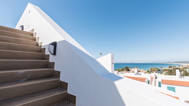 A staircase leading to a balcony with a clear view of the sea and surrounding buildings. - Prainha Luxury Apartment (Alvor)