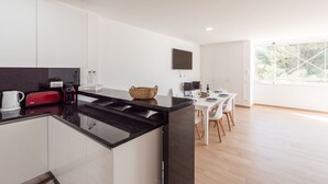 A modern kitchen with white cabinets, a black countertop, and a dining area with a white table and chairs. - Prainha Luxury Apartment (Alvor)
