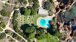 An aerial view of a resort with a swimming pool, landscaped areas, and rocky terrain. - Prainha Luxury Apartment (Alvor)