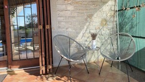 Un patio con dos sillas de metal, una mesita con un florero y una vela, y una pared de piedra.