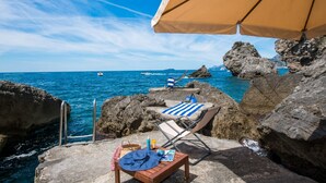 A beachside setting with a lounge chair and umbrella, rocky coastline, and a view of the sea. - Terrazze di Laurito, at 3 kms from Positano (Positano)