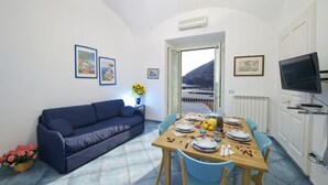 A dining area with a table set for four, a blue sofa, and a view of the sea through an open door. - Dolce Vita B by Amalfi Beaches (Amalfi)
