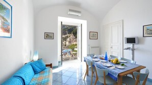 A bright room with a balcony, a dining table set with plates and glasses, and a sofa with a blue cover. - Dolce Vita B by Amalfi Beaches (Amalfi)