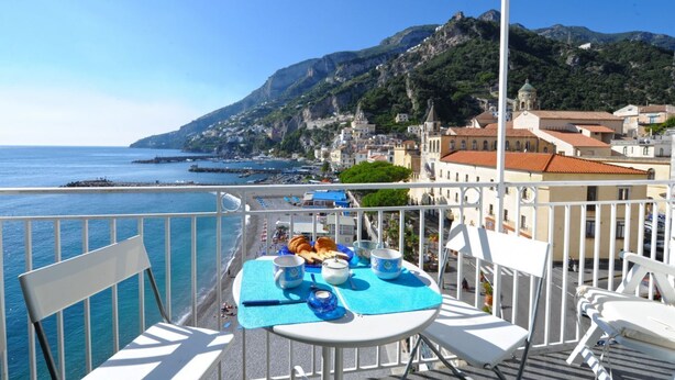 A balcony with a table set for breakfast overlooking a coastal town and the sea. - Dolce Vita B by Amalfi Beaches (Amalfi)