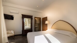 Ein Hotelzimmer mit einem großen Bett, einem an der Wand befestigten Fernseher, einem Holzschrank und einem Spiegel.