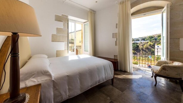 Ein Hotelzimmer mit Bett, Lampe, Stuhl und einem Balkon mit Blick.