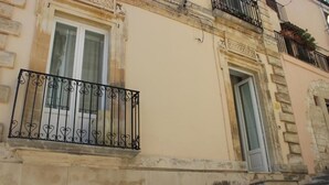 Eine Gebäudefassade mit rustiziertem Sockel, einem Balkon mit schmiedeeisernen Geländern und einer Tür mit Glasfenster.