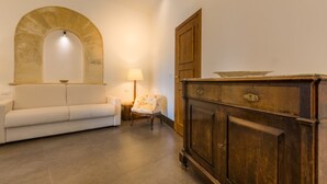 Ein Zimmer mit einem weißen Sofa, einem Holzkabinett, einer Lampe und einem Steinbogen.