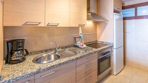 Una cocina moderna con armarios de madera, encimera de granito, pileta de acero inoxidable, horno integrado y refrigerador.