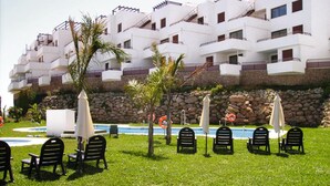 Zona junto a la piscina con mobiliario exterior y vistas a un edificio de varios pisos.