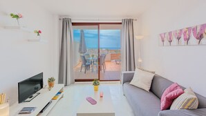 Una sala de estar moderna con televisor de pantalla plana, una mesa de centro, un sofá y un balcón con vista al mar.