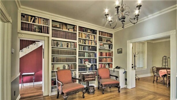 Eine Bibliothek mit Bücherregalen, zwei Stühlen, einem Tisch und einer Treppe.