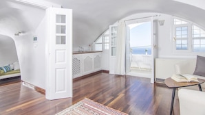 Una habitación amplia con piso de madera, paredes blancas y un ventanal con vistas al mar.