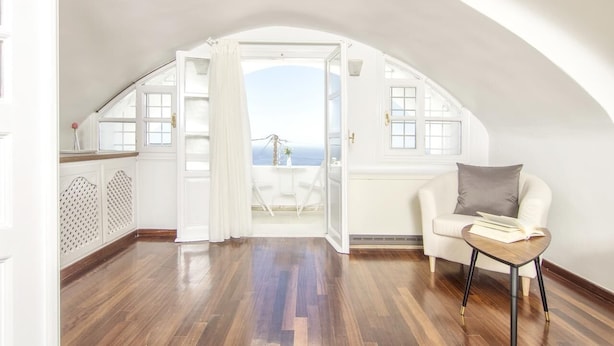 Una habitación amplia con un techo abovedado, un sofá blanco, una mesita y vistas al mar a través de una puerta abierta.