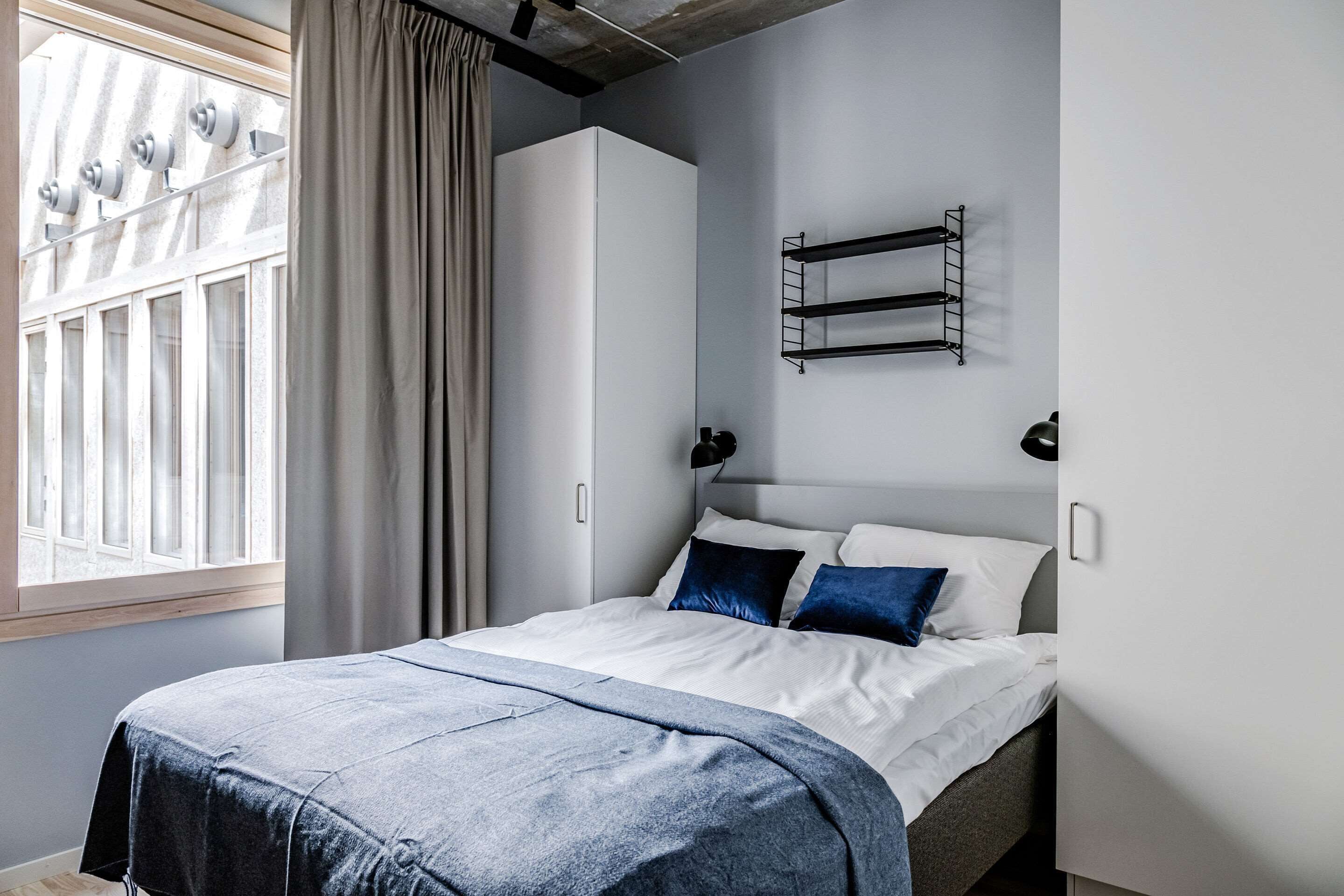 Una camera da letto moderna con un letto, una finestra con tende, un armadio e una mensola a parete.