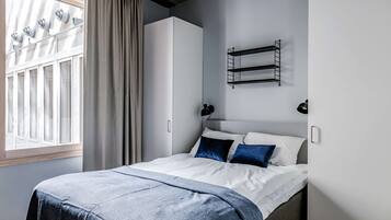 Una camera da letto moderna con un letto, una finestra con tende, un armadio e una mensola a parete.