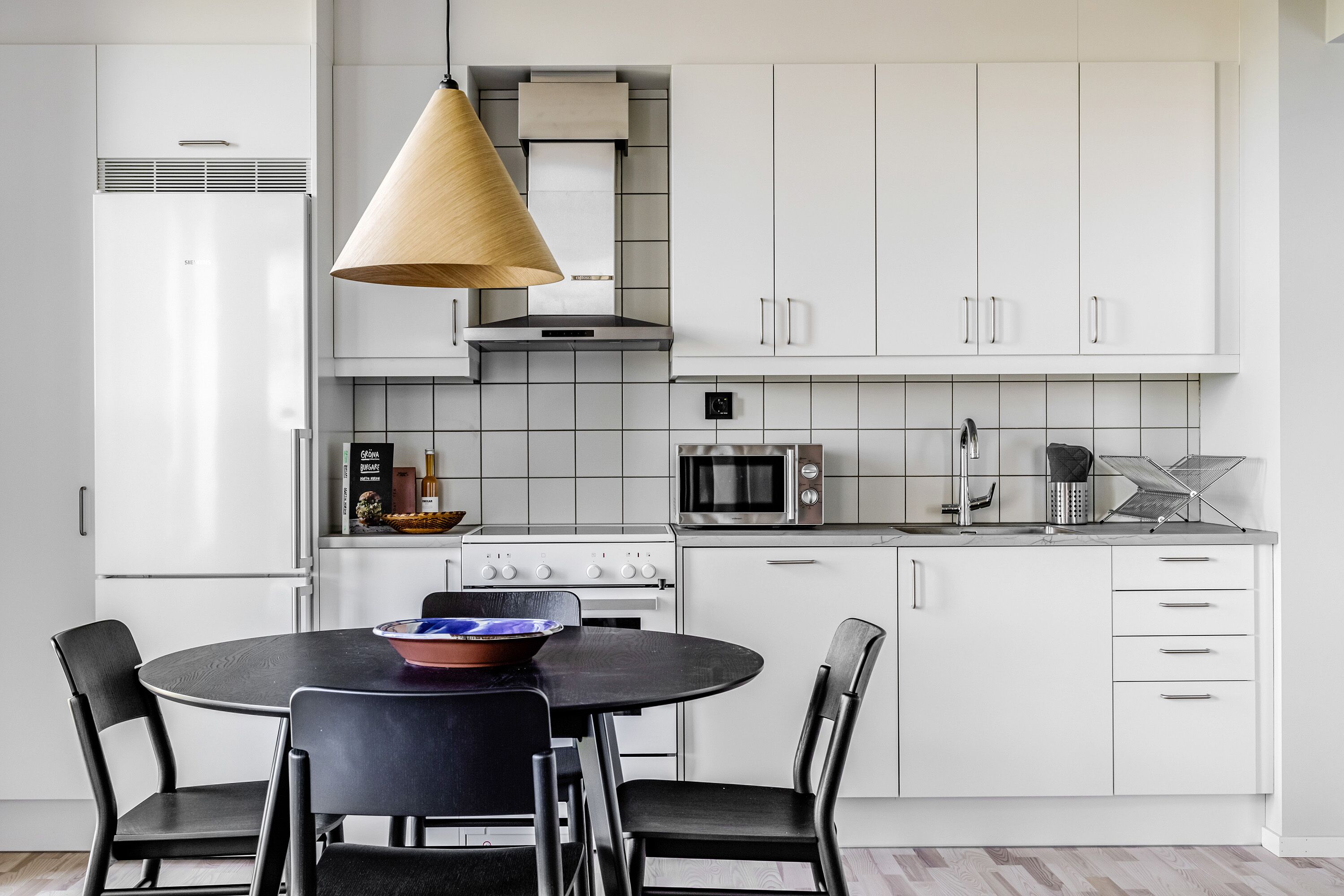 A modern kitchen with white cabinets, a stove, microwave, and a hanging light fixture.