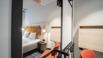 Una camera d'albergo compatta con un letto, una scrivania, due sedie e uno specchio.