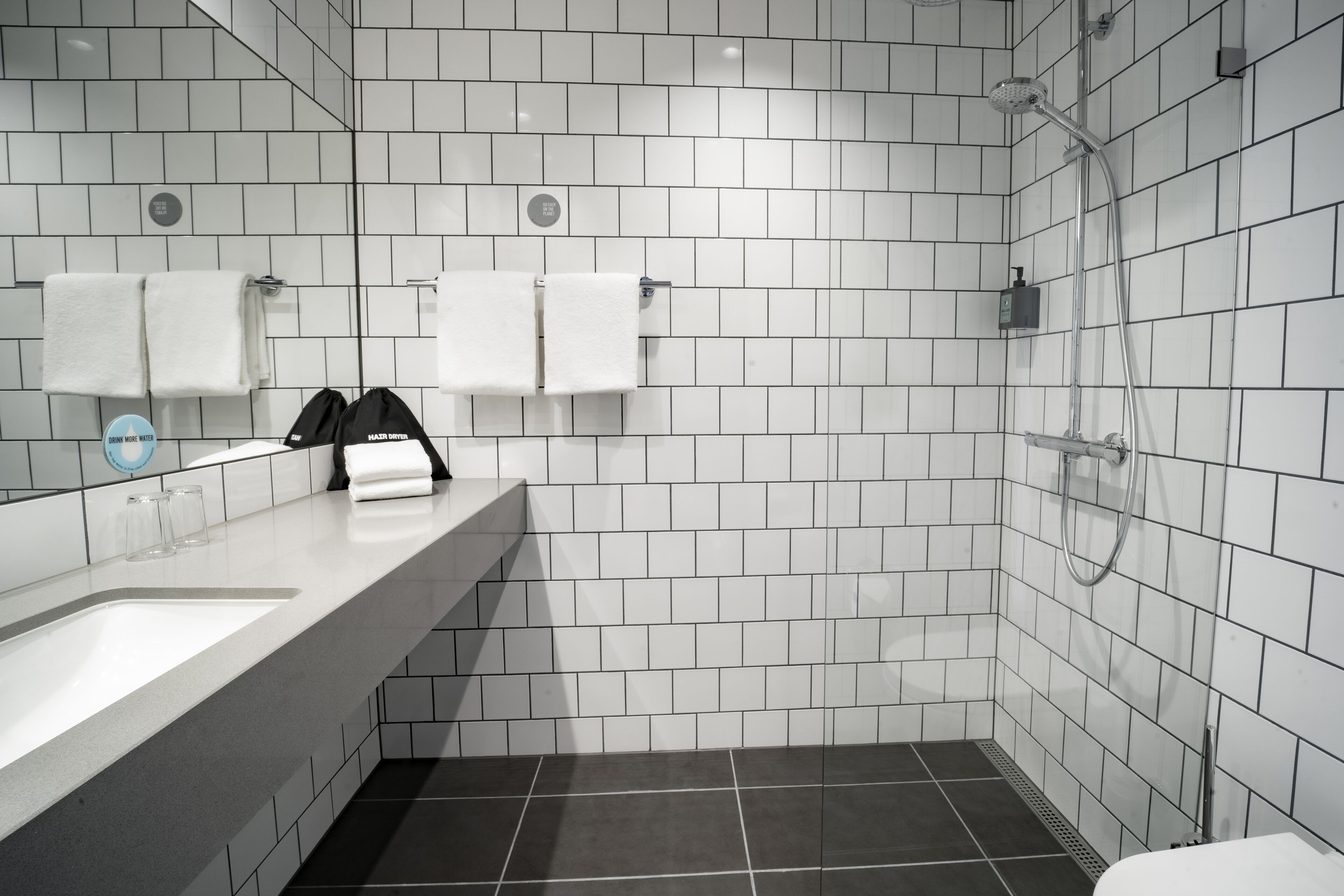 Un baño moderno con paredes de azulejos blancos, un lavabo con espejo y una zona de ducha.