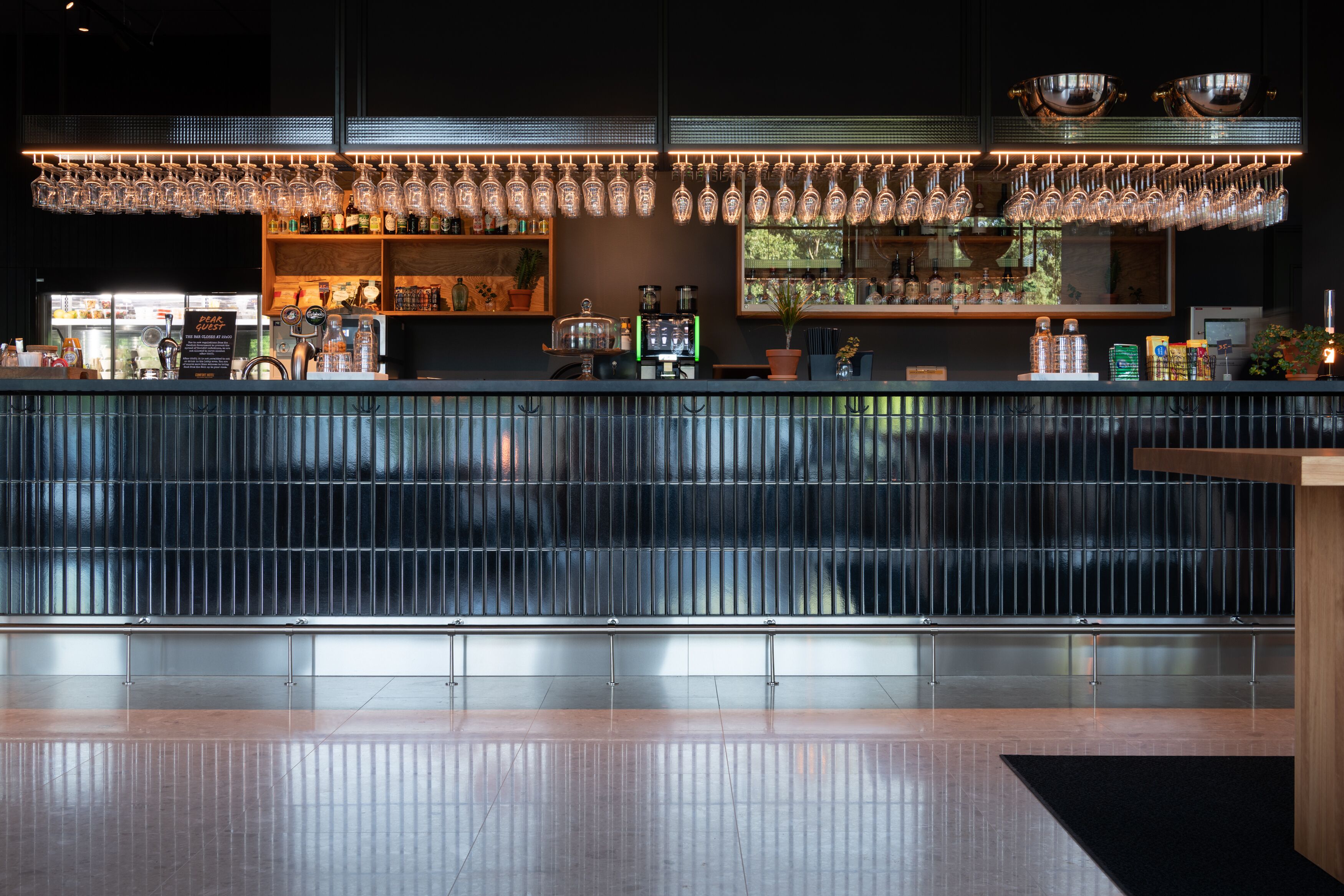 A modern bar area with a long counter, hanging light fixtures, and a variety of bar tools and bottles.