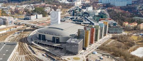 An aerial view of a cityscape with a large stadium, multiple high-rise buildings, and a complex railway system.