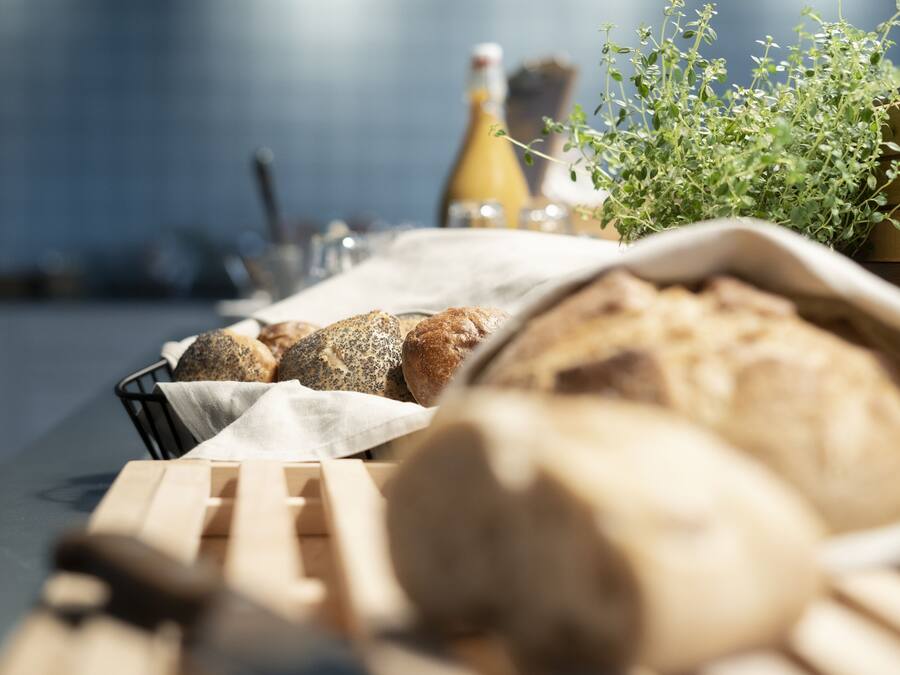 Un panier de pain est posé sur une table, avec une bouteille et une plante en arrière-plan.