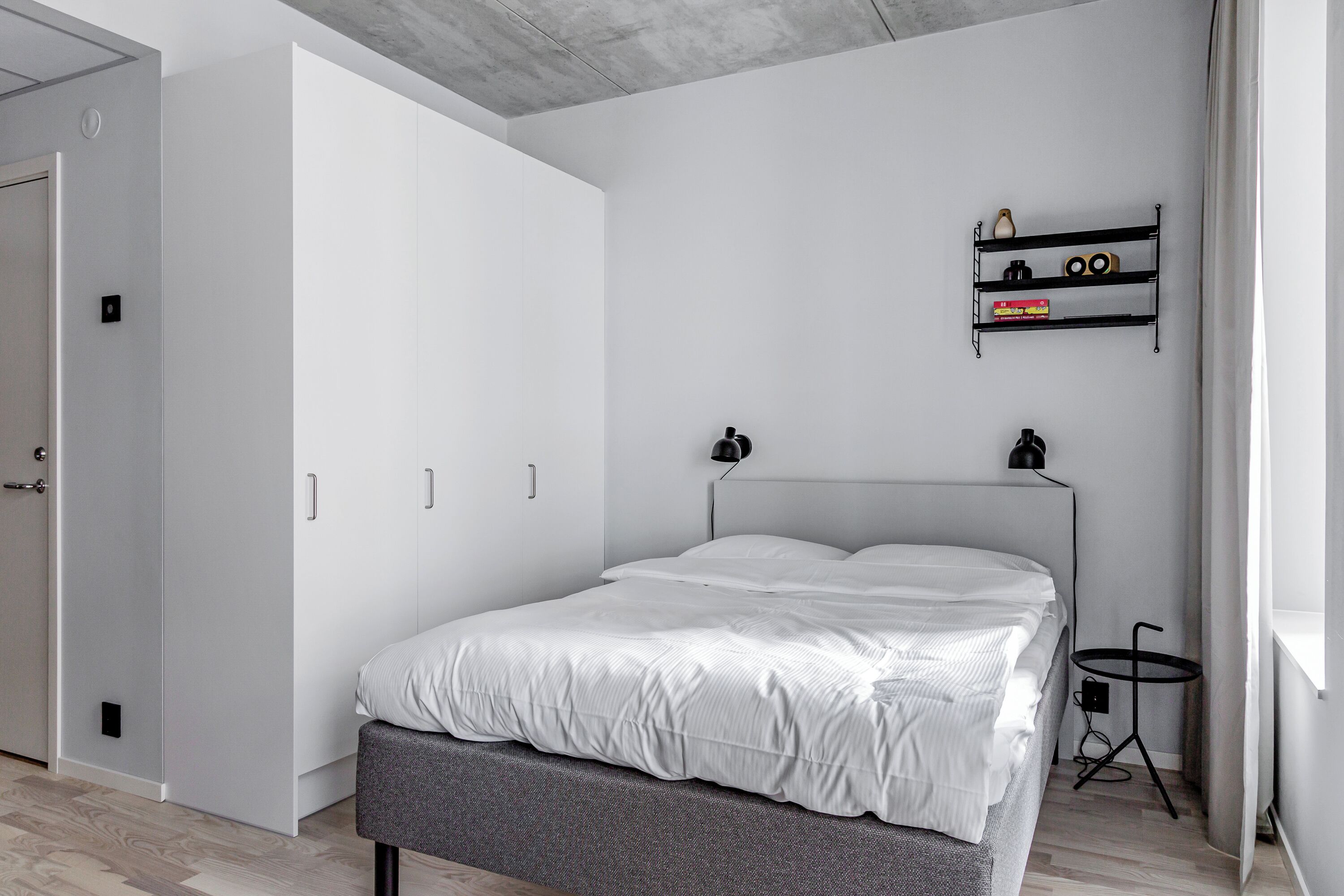 A modern bedroom with a bed, wardrobe, and a small table with a lamp.
