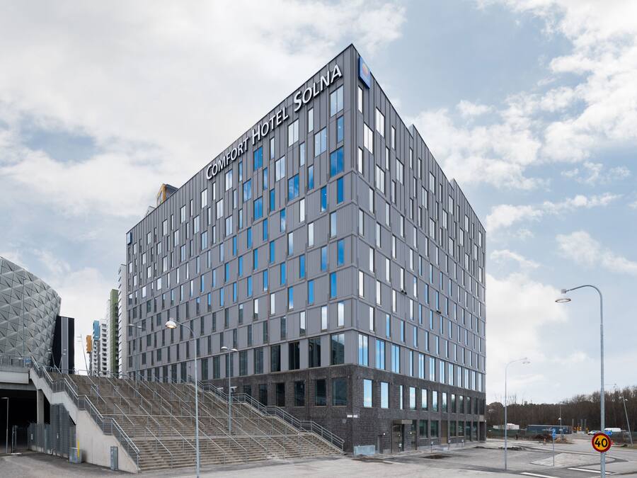 Un edificio moderno del Comfort Hotel con un letrero llamativo, una escalera que lleva a la entrada y una vista despejada del entorno.