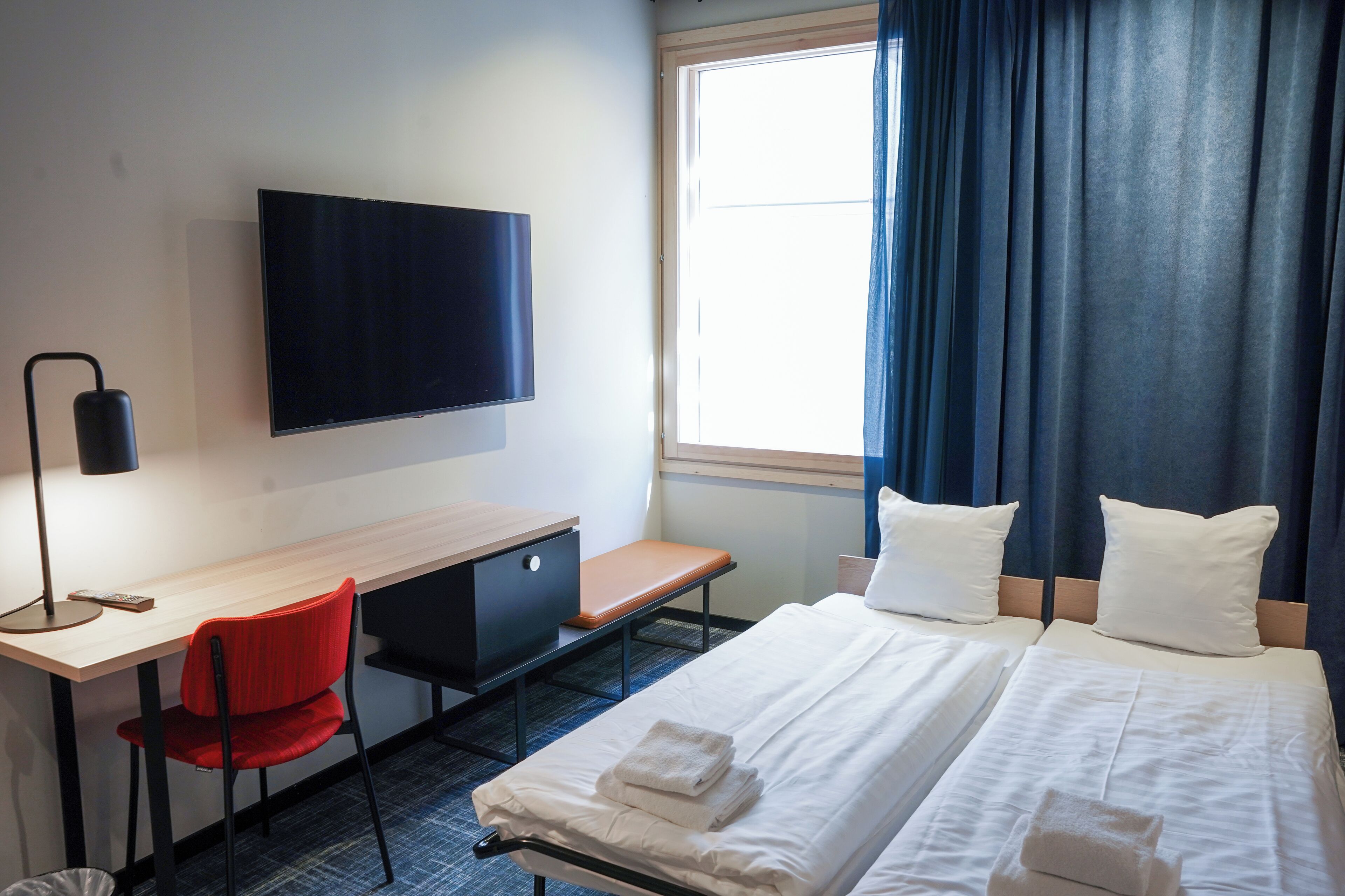 A hotel room with a bed, a desk, a chair, a TV, and a window with curtains.
