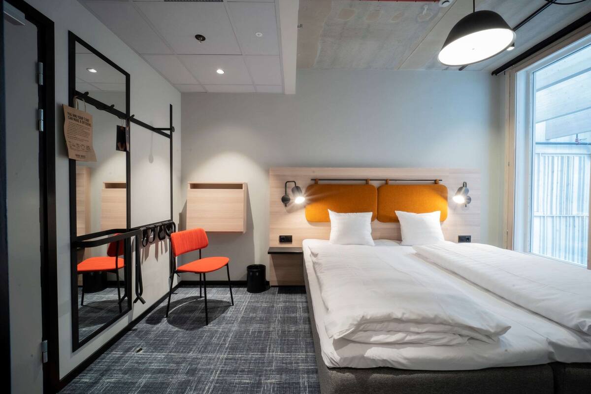 Ett hotellrum med en stor säng, ett skrivbord med en stol, en spegel och ett fönster med utsikt.