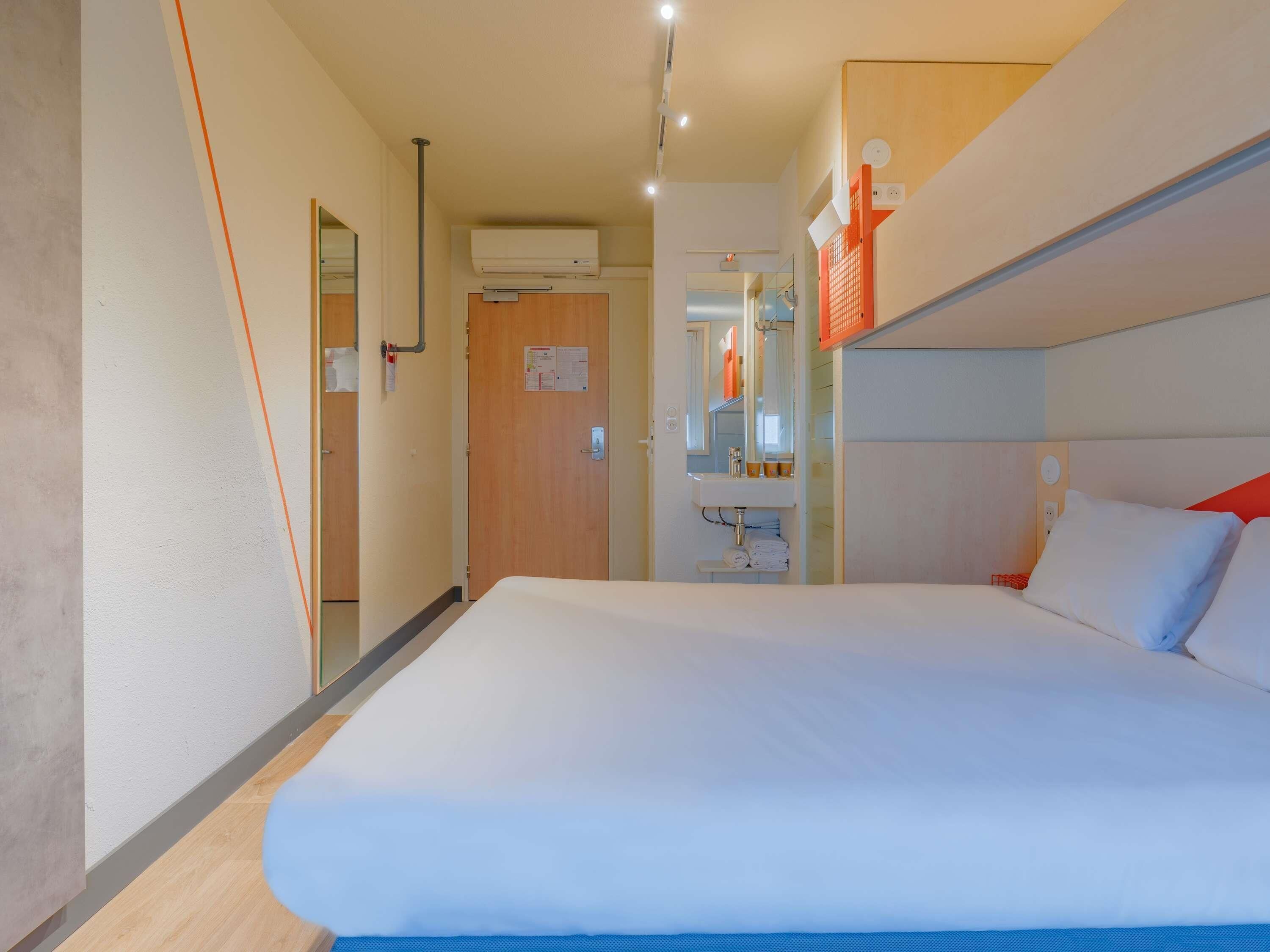 A hotel room with a large bed, a bathroom with a sink and mirror, and a door leading to another room.