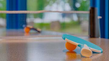 Une table de ping-pong avec un filet au milieu, une raquette bleue et orange, et un arrière-plan extérieur flou.