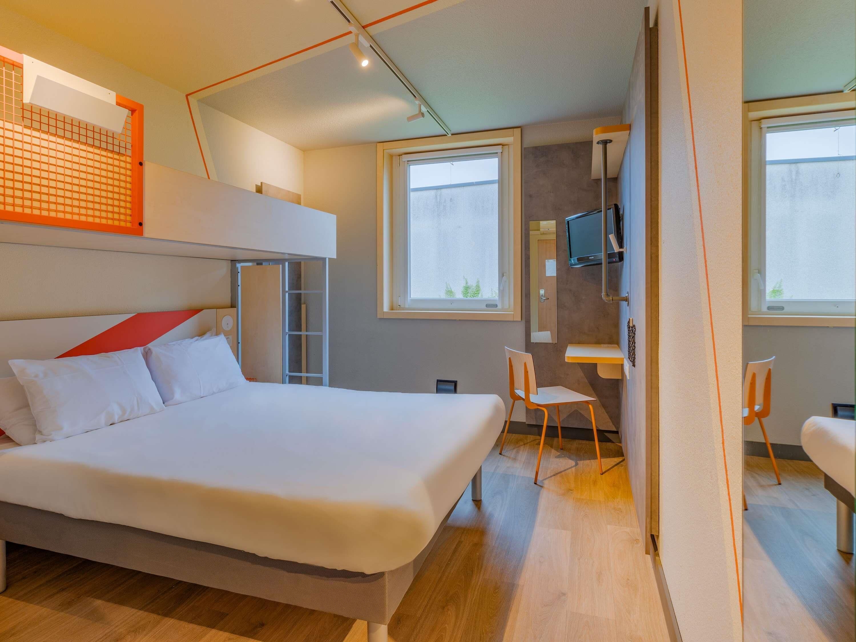 Una camera d'albergo moderna con un letto a castello, una scrivania, una sedia e una televisione.