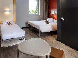 Quarto de hotel com duas camas, uma mesa pequena e uma cadeira. Há uma janela com vista para o verde lá fora.