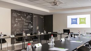 Un salón de conferencias con una larga mesa, sillas, tarjetas de identificación, botellas de agua y una pantalla de presentación que muestra 'ibis budget' y 'ibis styles'.